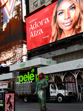 Adora Aiza in front of her first featured New York City Billboard. Adora says that it is her 5 year old dream come true as she watches with her pjs before heading to a flight for a show out in Europe.